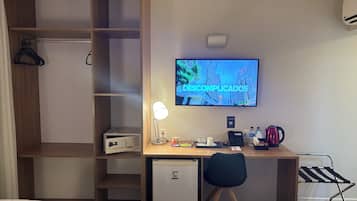 Habitación de hotel con escritorio, televisión, mini refrigerador, tetera y cama.