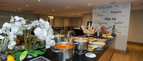 A buffet area with various food items and a sign listing the menu in Portuguese.