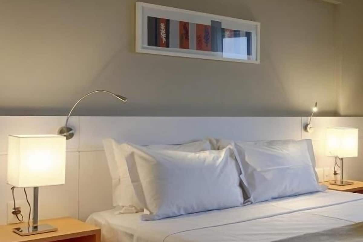 Habitación de hotel con una cama, dos lámparas de noche, una mesita de noche y una obra de arte colgada en la pared.