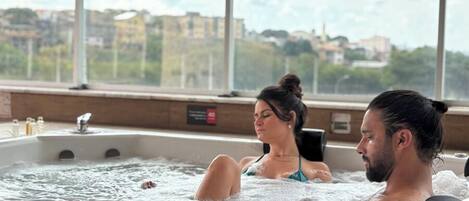Um casal relaxando em uma banheira de hidromassagem com vista para a cidade.