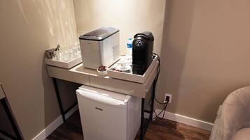 Uma cozinha compacta com cafeteira, mini-geladeira e um recipiente de vidro na bancada.