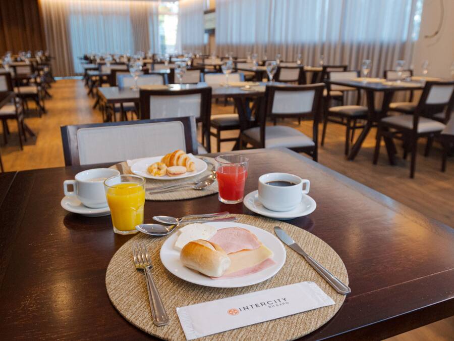 A hotel dining area with tables set for breakfast, including croissants, ham, cheese, and juice.