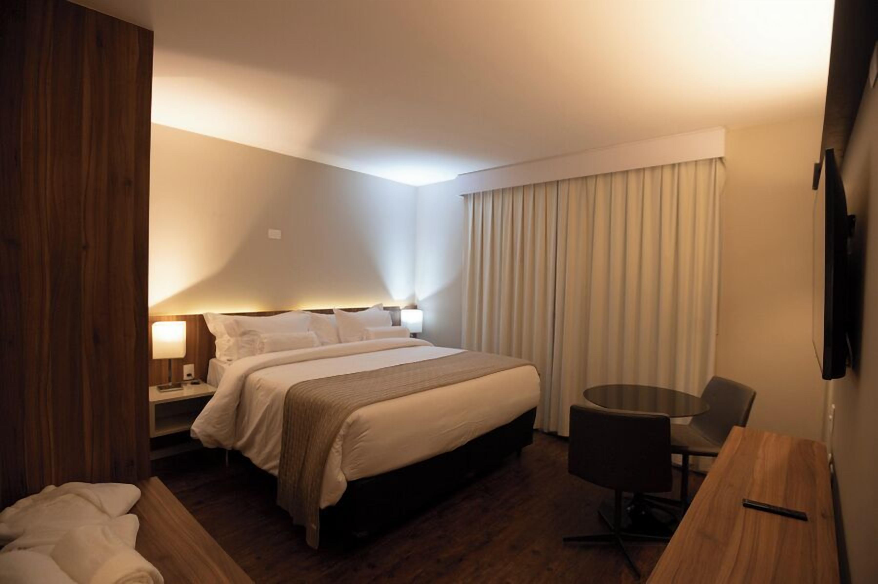 A hotel room with a large bed, bedside tables, a desk, and a chair.