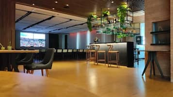 Un área de bar moderna con suelo de madera, taburetes y una televisión que muestra un paisaje urbano.
