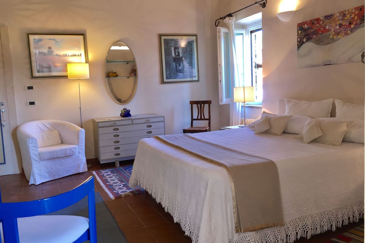 Ein Schlafzimmer mit einem großen Bett, einem Sessel, einem Schminktisch und einem Spiegel.