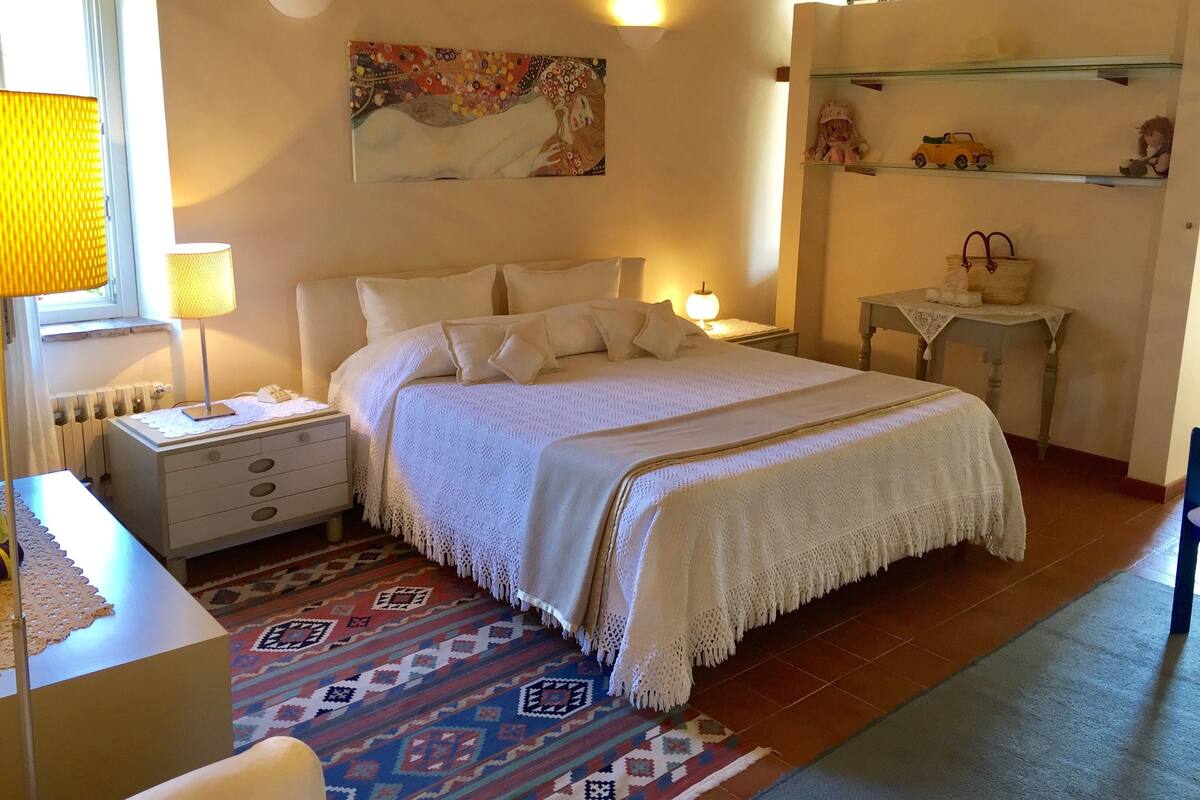Ein ordentlich eingerichtetes Schlafzimmer mit Bett, Nachttischen, einer Lampe, einem Bild und einem Regal mit Dekoration.