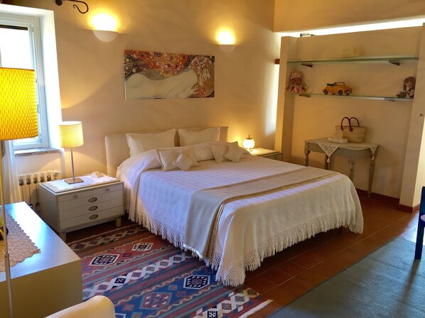 Une chambre avec un grand lit, des tables de chevet, une commode, une lampe, un tableau au mur et une étagère avec des objets décoratifs.
