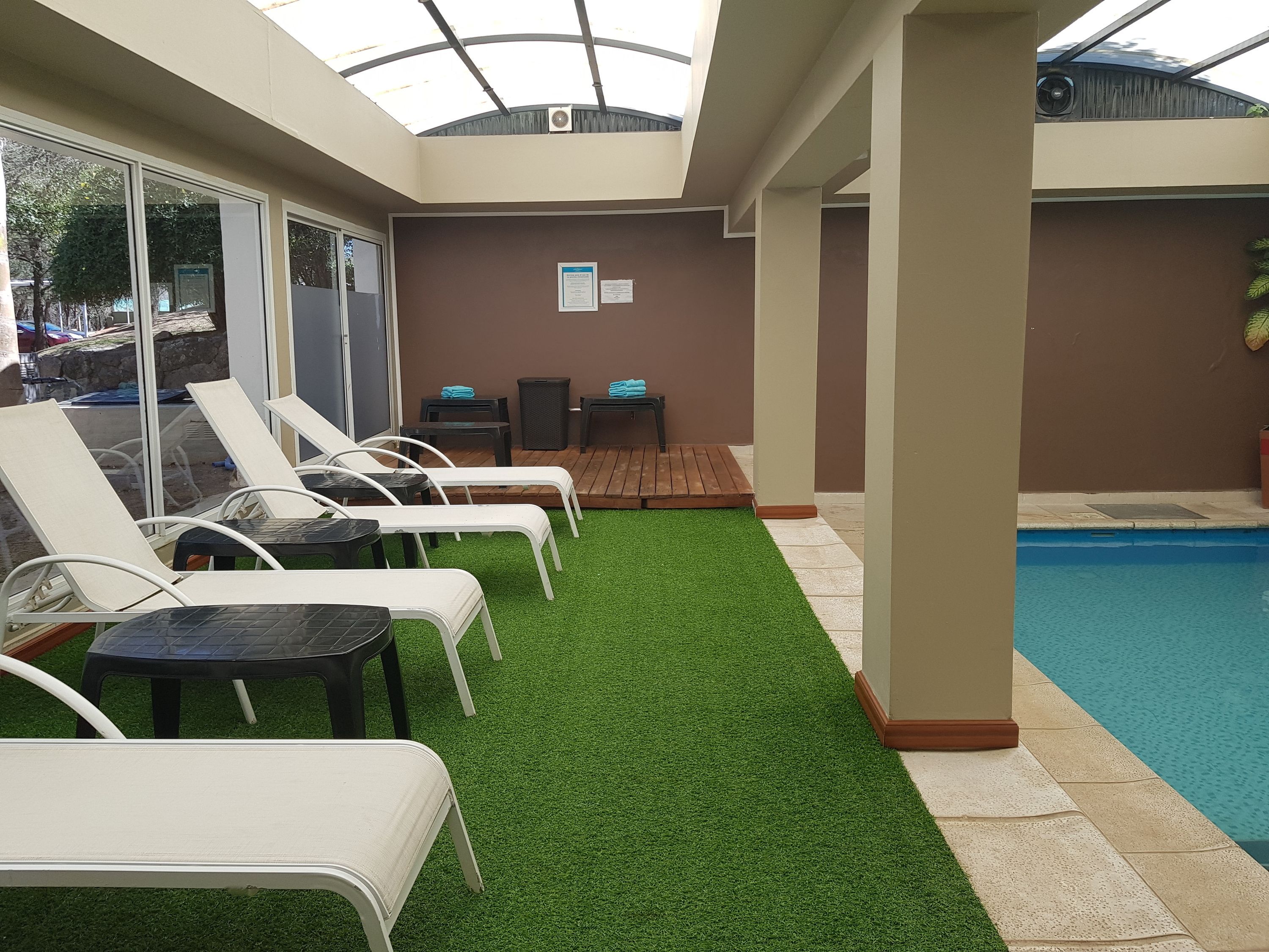 Zona de piscina con césped artificial, sillas de descanso y un área de estar techada.