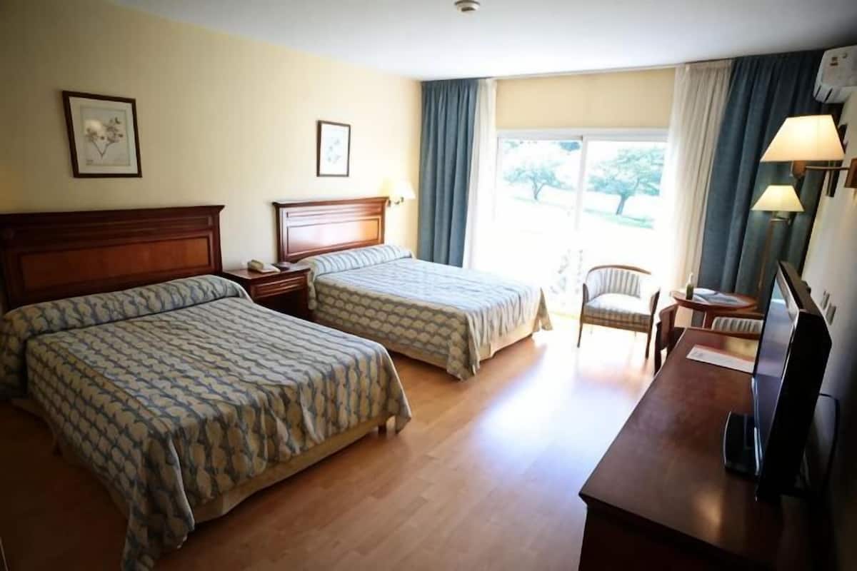 A hotel room with two beds, a desk, a chair, and a window with curtains.