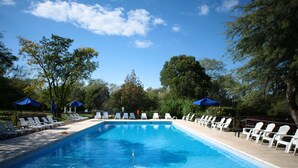 A rectangular swimming pool with clear blue water, surrounded by white lounge chairs and blue umbrellas. - Howard Johnson by Wyndham, Villa General Belgrano (Villa General Belgrano)