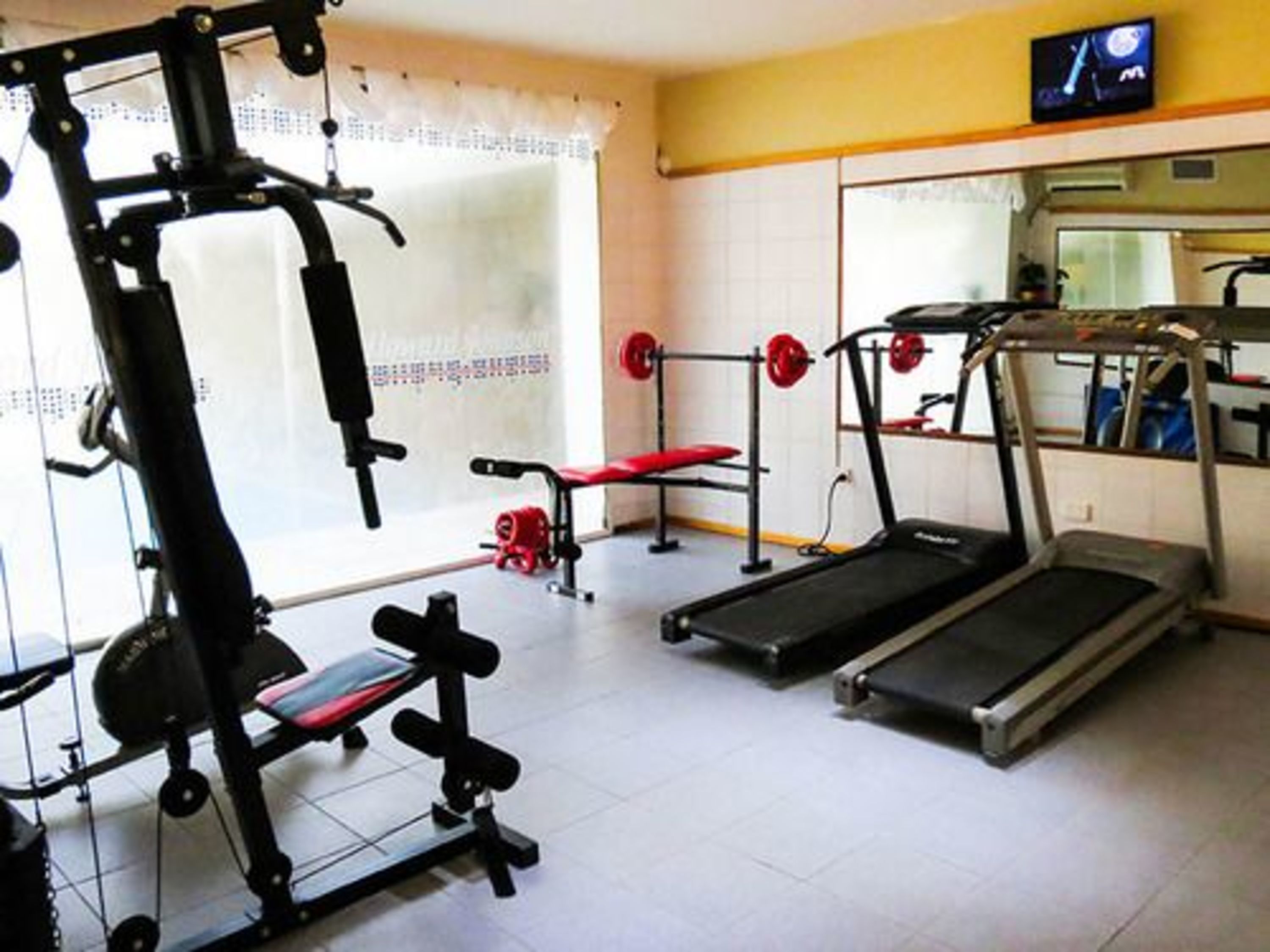 Un gimnasio con cinta de correr, banco de pesas y varias máquinas de ejercicio.