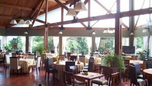 A spacious indoor dining area with multiple tables and chairs, large windows, and a high ceiling with exposed beams. - Howard Johnson by Wyndham, Villa General Belgrano (Villa General Belgrano)