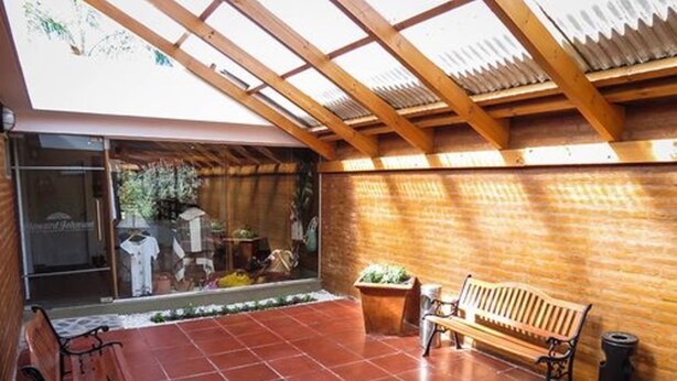 Un patio couvert avec un banc en bois et une poubelle.