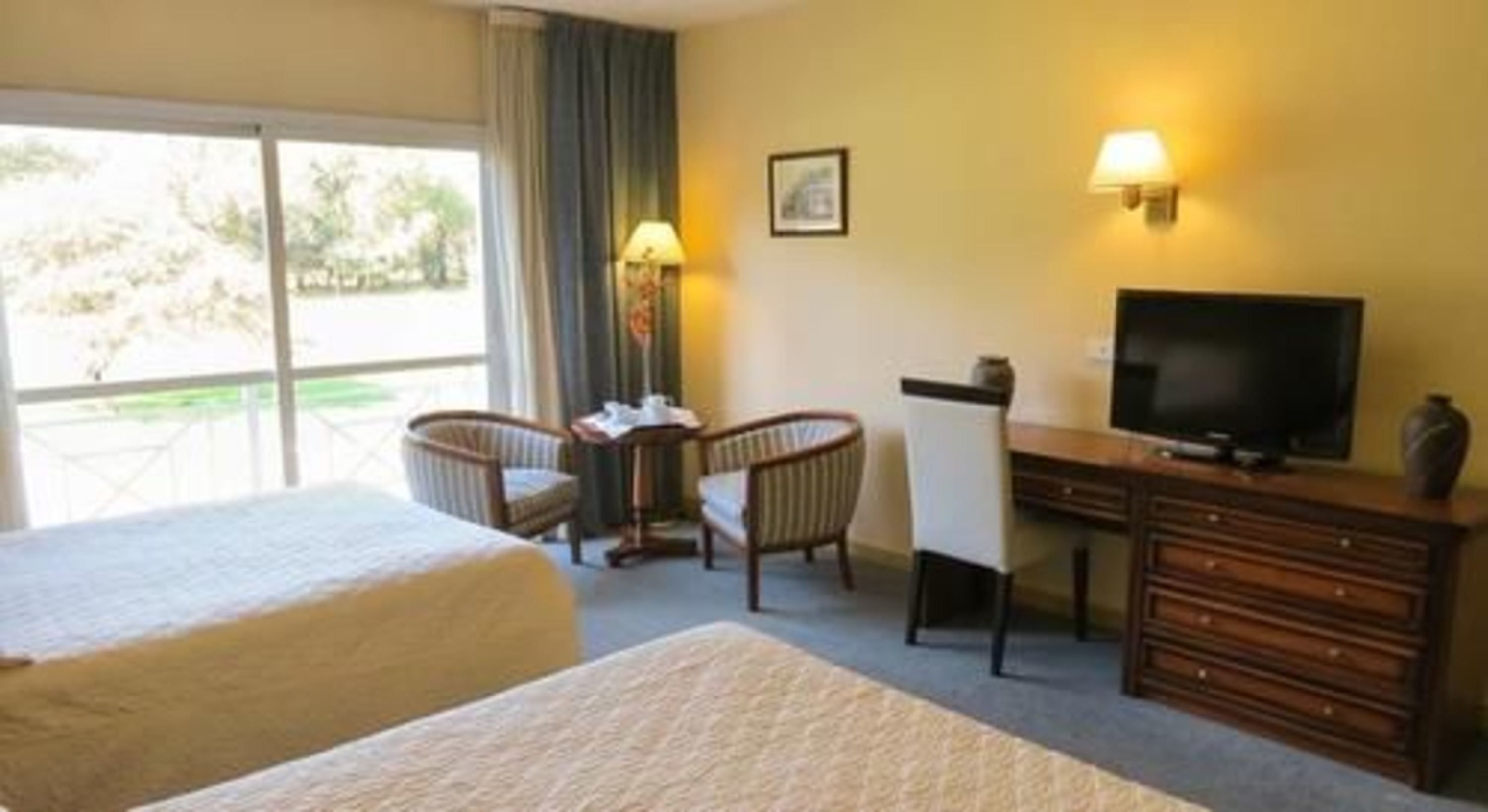 A hotel room with two beds, a desk with a television, a chair, and a lamp.
