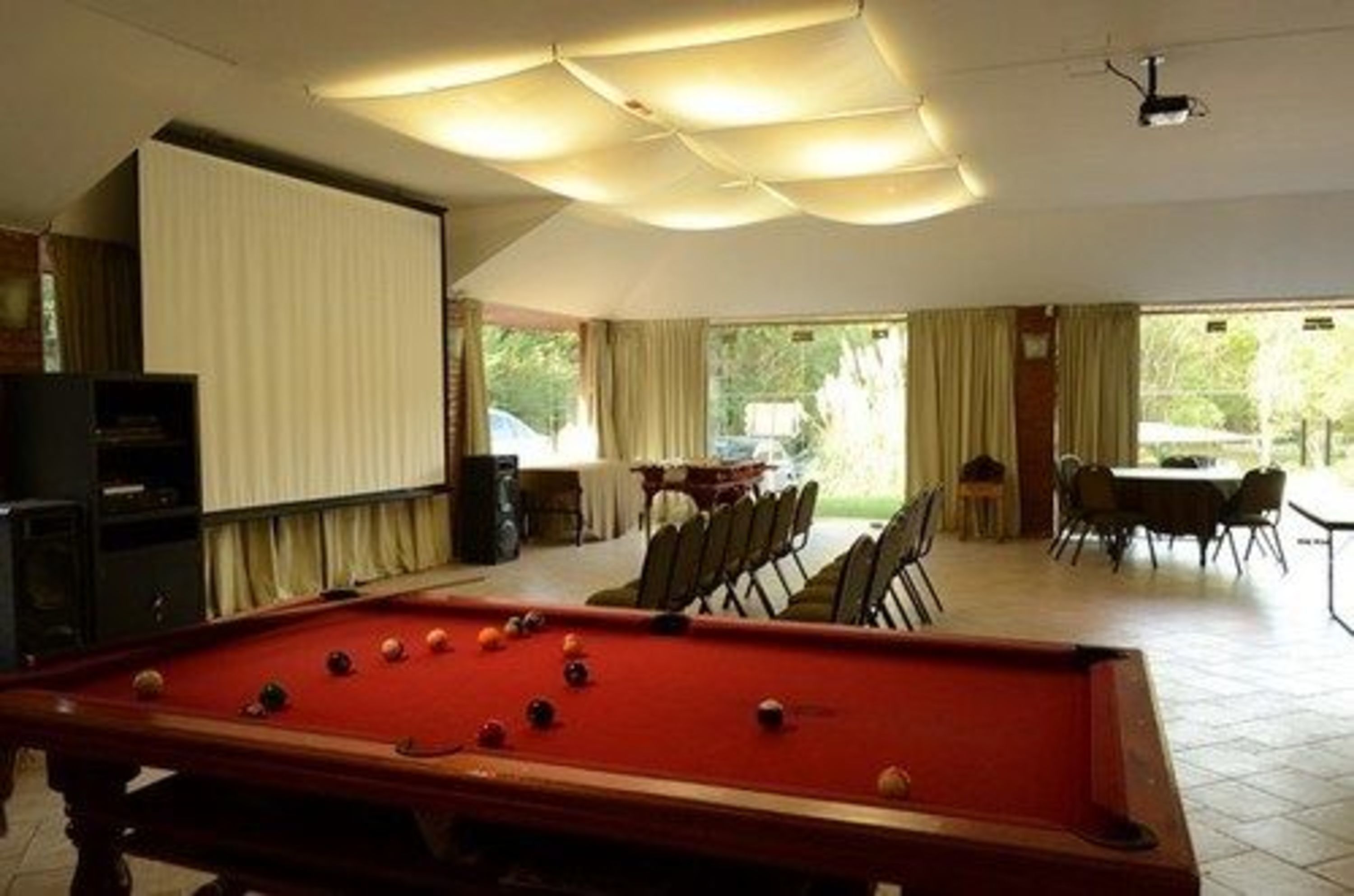 Ein Billardtisch in einem Raum mit Projektor, Essbereich und großen Fenstern.
