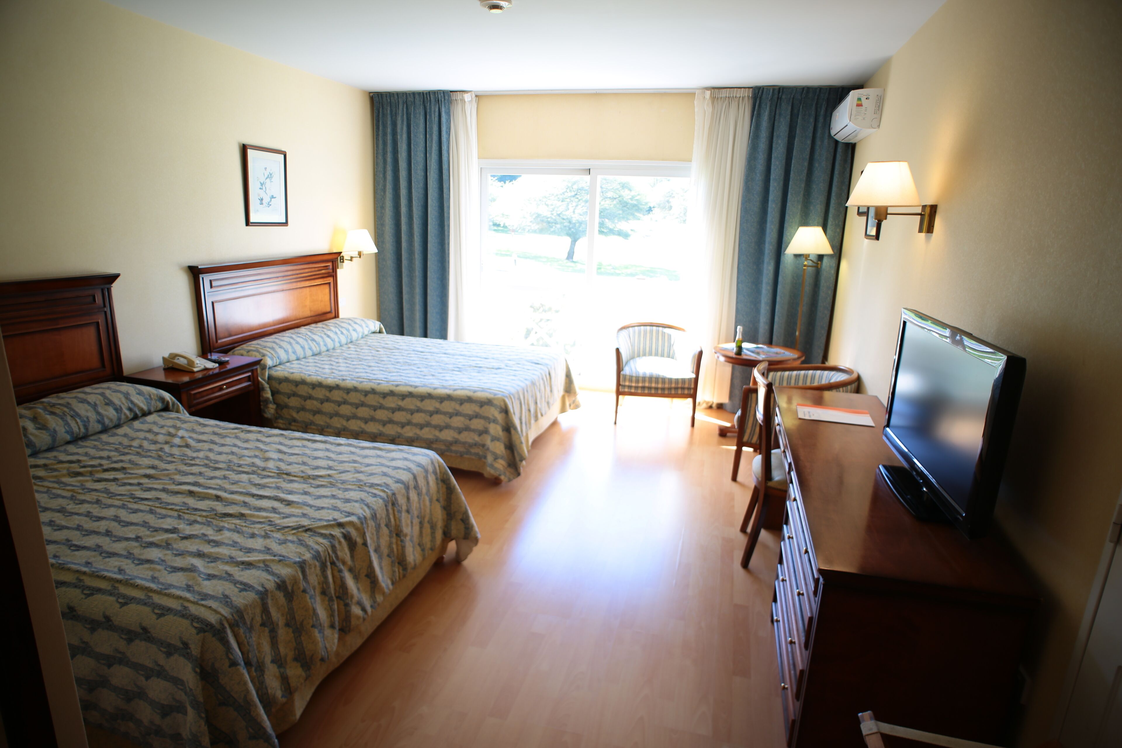 Une chambre d’hôtel avec deux lits, un bureau avec une télévision, une chaise et une fenêtre avec des rideaux.
