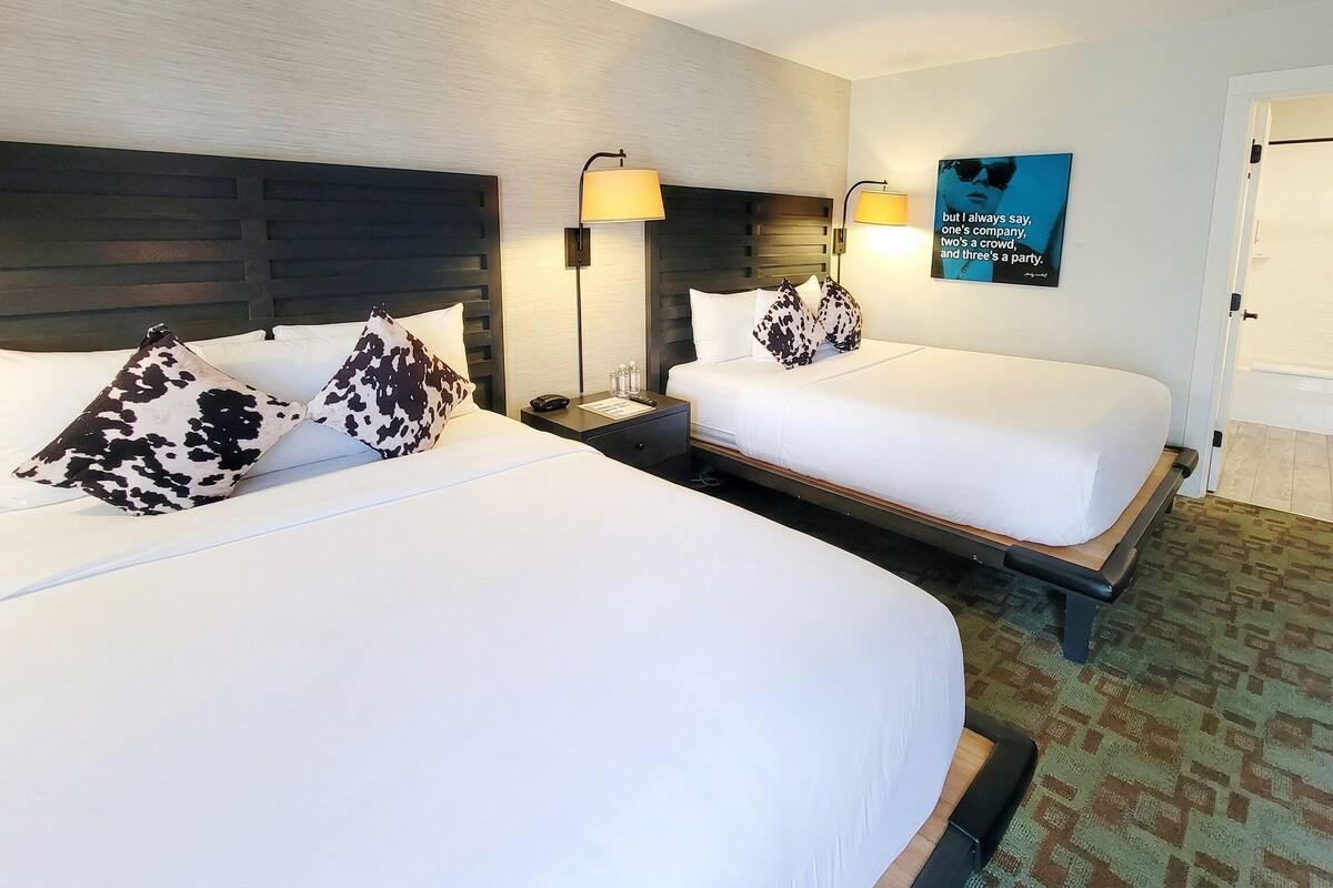 A hotel room with two beds, a headboard, bedside lamps, a wall art piece, and a patterned carpet.