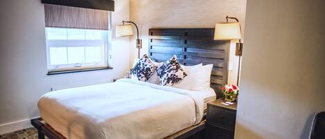 A hotel room with a bed, bedside lamps, a nightstand, and a window with blinds.
