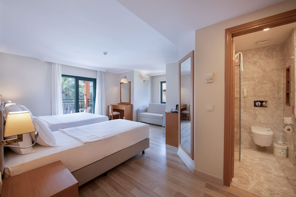 A hotel room with a large bed, bedside table, lamp, and a view of the outside.