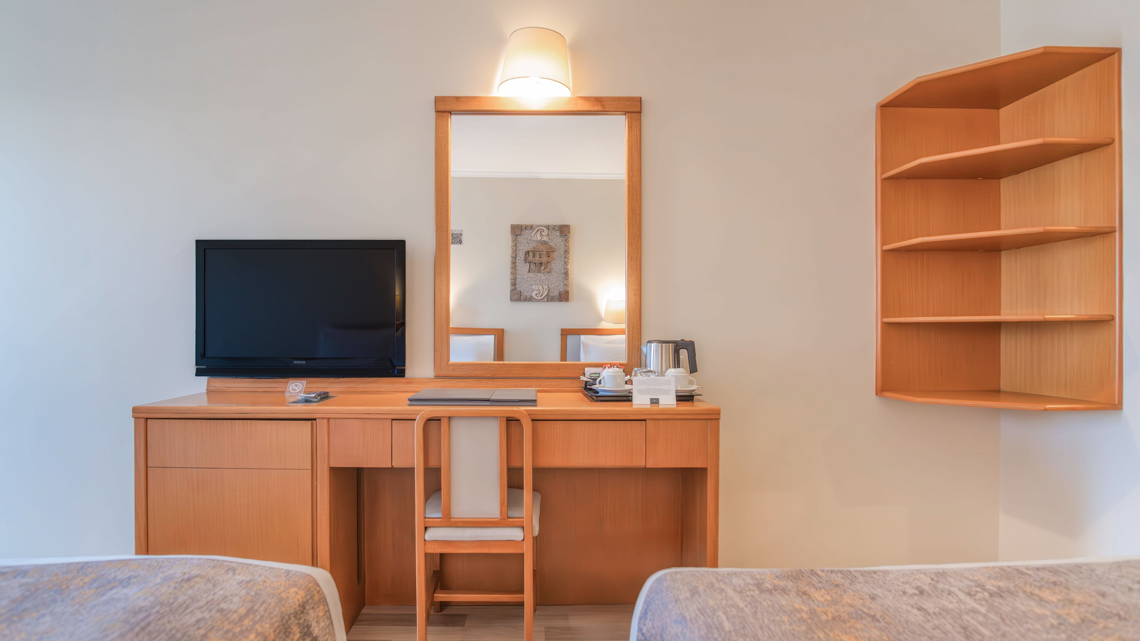 A hotel room with a wooden desk, a television, a chair, a bed, and a shelf.