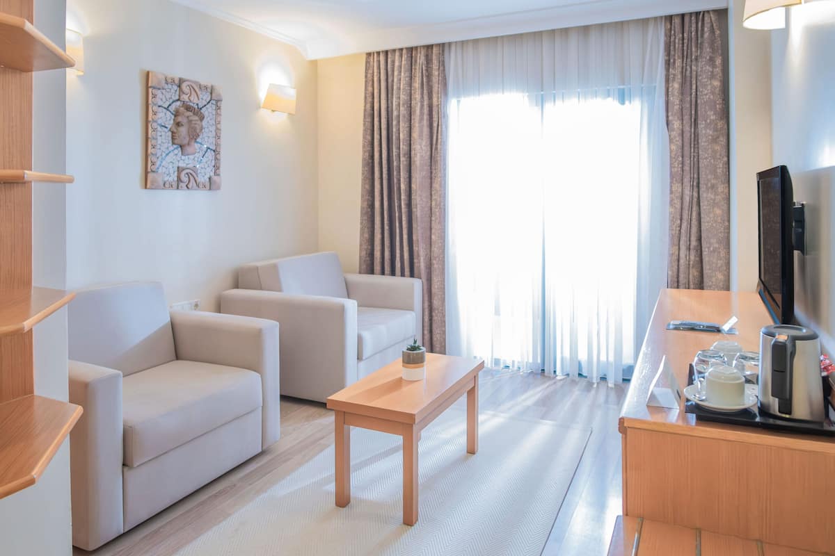 A modern hotel room with a sofa set, a wooden coffee table, a TV, and a minibar.