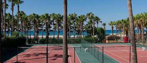 A tennis court surrounded by palm trees and a clear blue sky.