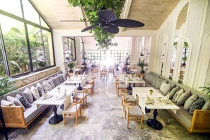 A spacious dining area with high ceilings, large windows, and a ceiling fan. Tables and chairs are arranged for dining. - Miramare Queen Hotel - All Inclusive (Manavgat)