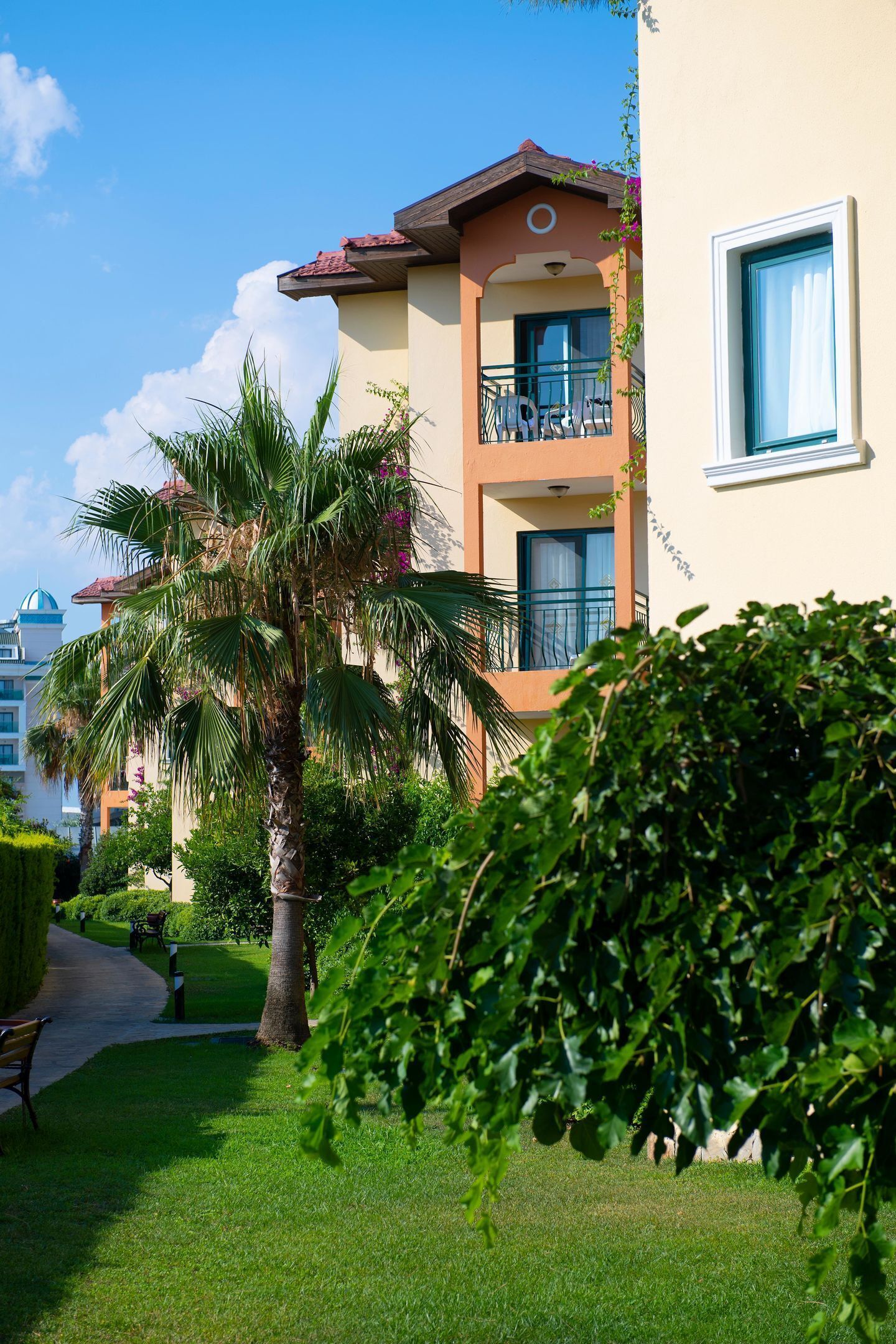 A hotel with a balcony, a palm tree, and a well-maintained lawn.