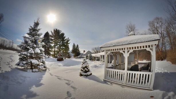 A snow-covered gazebo with a clear view of the surrounding trees and a bright sun in the background. - Harwood Hill Motel (Bennington)