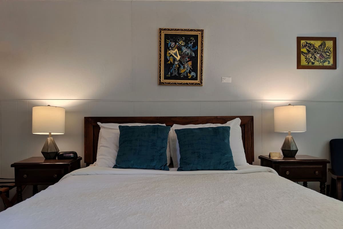 A hotel room with a large bed, two bedside tables with lamps, and two framed artworks on the wall.