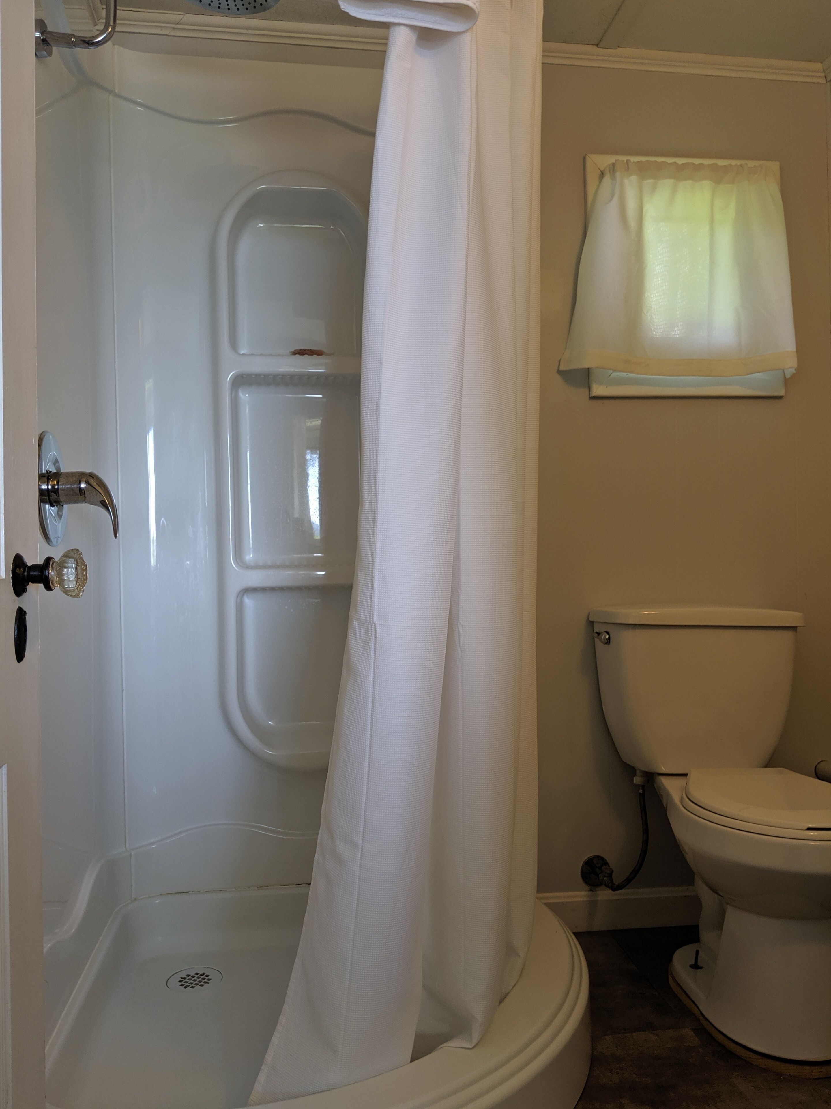 A bathroom with a shower, toilet, and a window with a curtain.