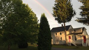 A house with a red door and windows, surrounded by trees and a rainbow in the sky. - Harwood Hill Motel (Bennington)