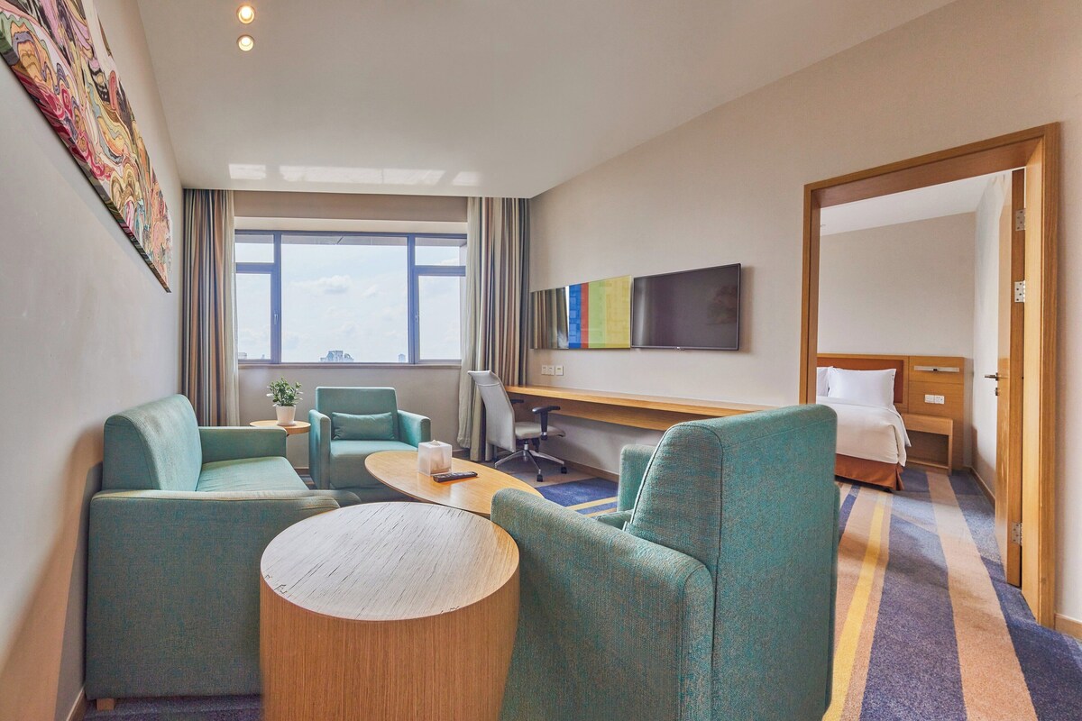 A hotel room with a sofa, armchairs, a small table, a TV, a desk, and a bed.