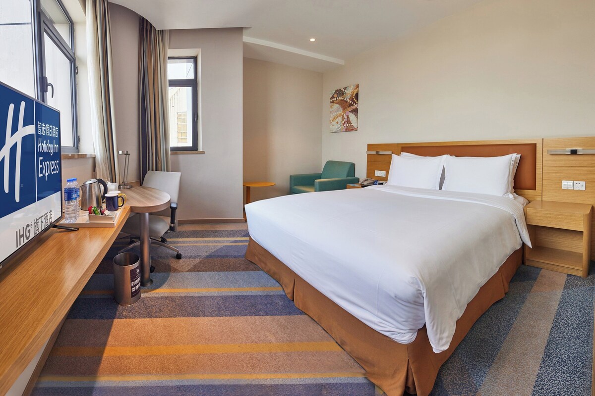 A hotel room with a bed, a desk, a chair, a small table, and a window.
