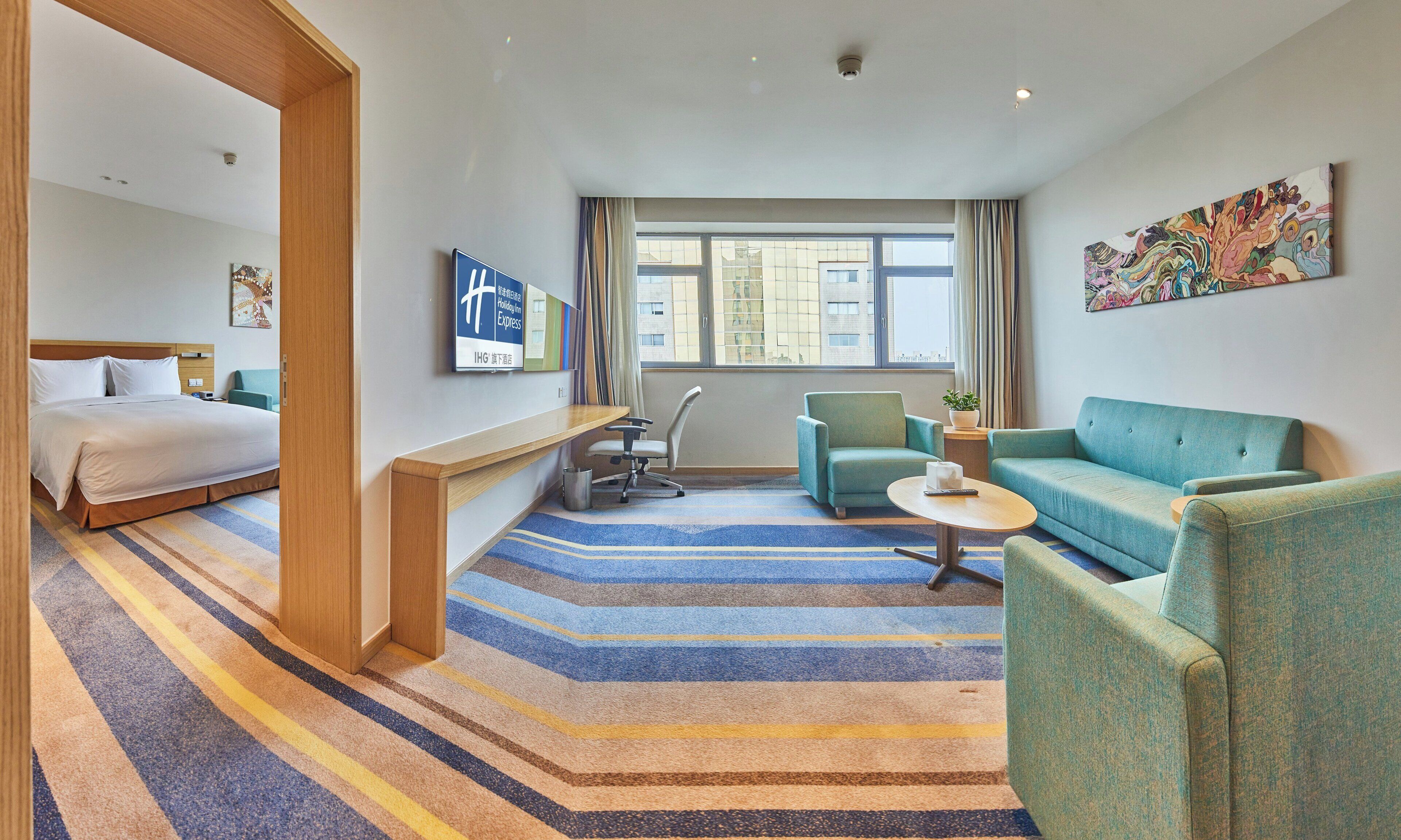 A hotel room with a bed, a desk, a chair, a sofa, a coffee table, and a large window.