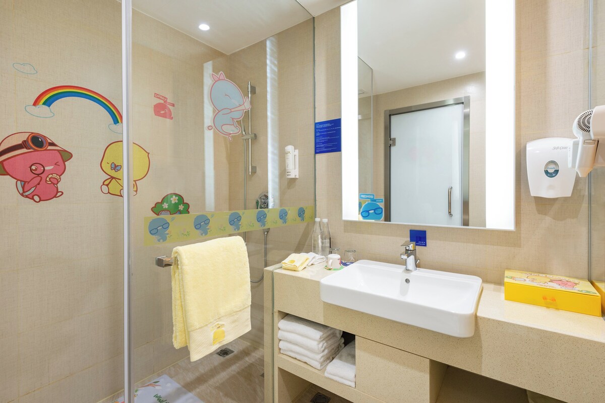 A bathroom with a white sink, mirror, and glass shower enclosure. There are cartoon stickers on the walls and a yellow towel rack.