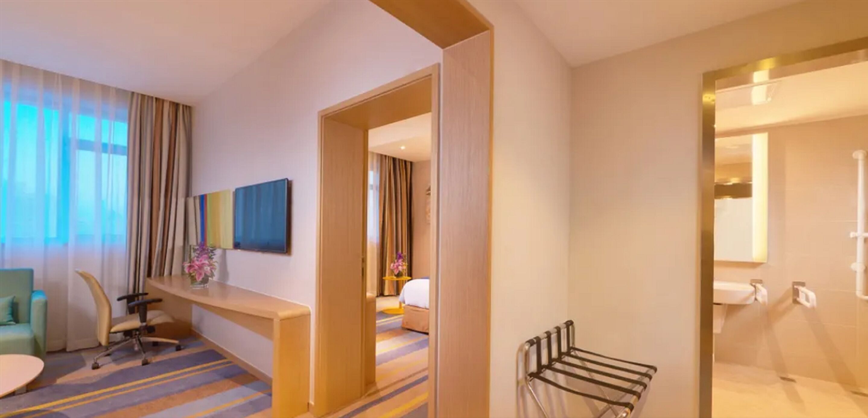 Een hotelkamer met een bureau, stoel, bed en een badkamer met wastafel en handdoekhouder.