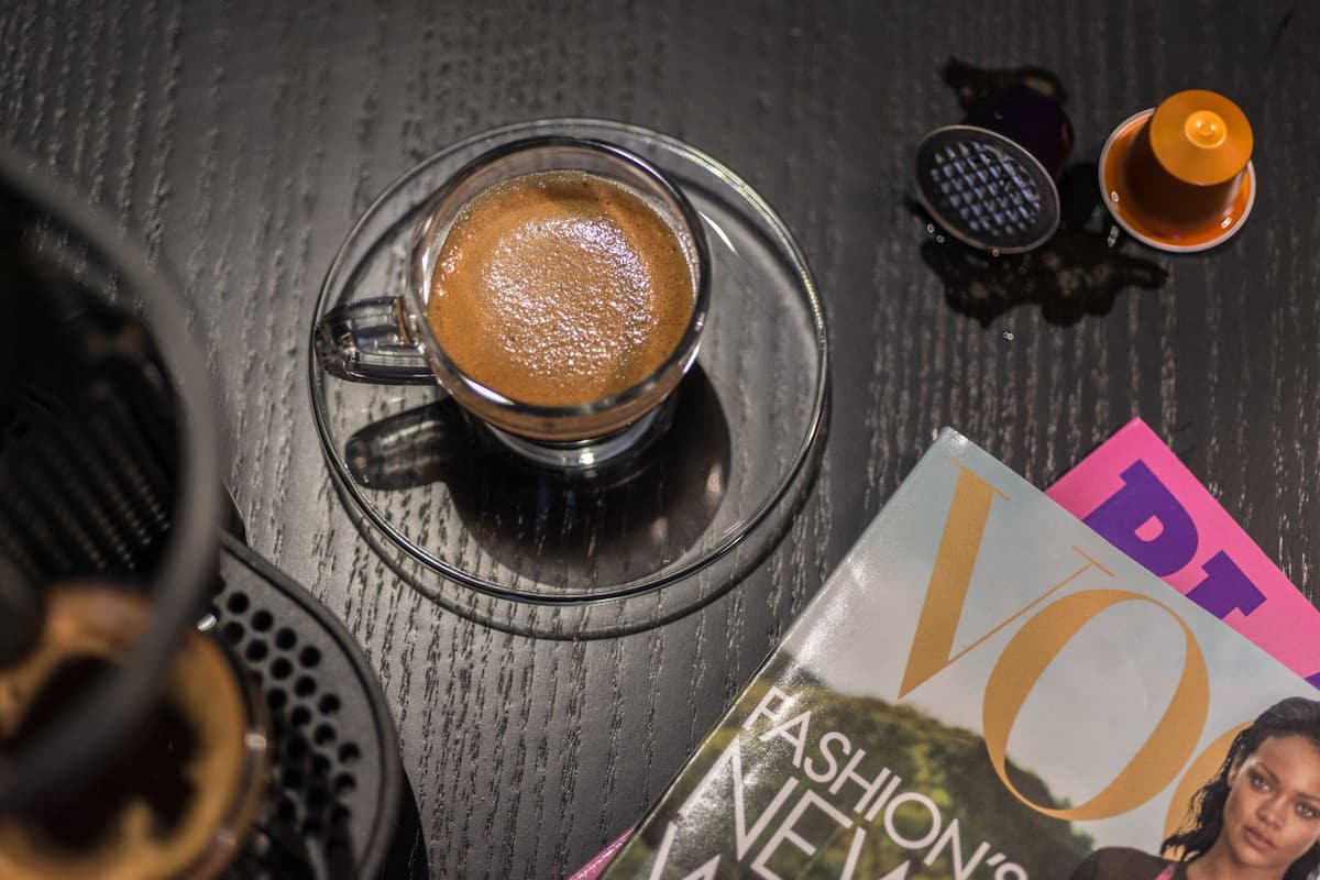 A table with a cup of coffee, a magazine, and a teapot.
