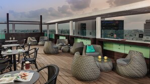 A rooftop bar with wicker furniture, tables with drinks, and a city view. - NYX Tel Aviv (Tel Aviv)