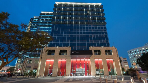 A modern hotel with a prominent glass facade and a red-lit entrance. - NYX Tel Aviv (Tel Aviv)