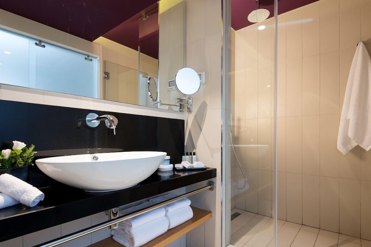 A modern bathroom with a large white sink, a mirror, and a glass shower enclosure.