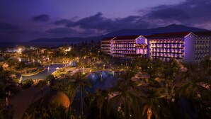 Un hotel grande con varios pisos, piscina y palmeras.