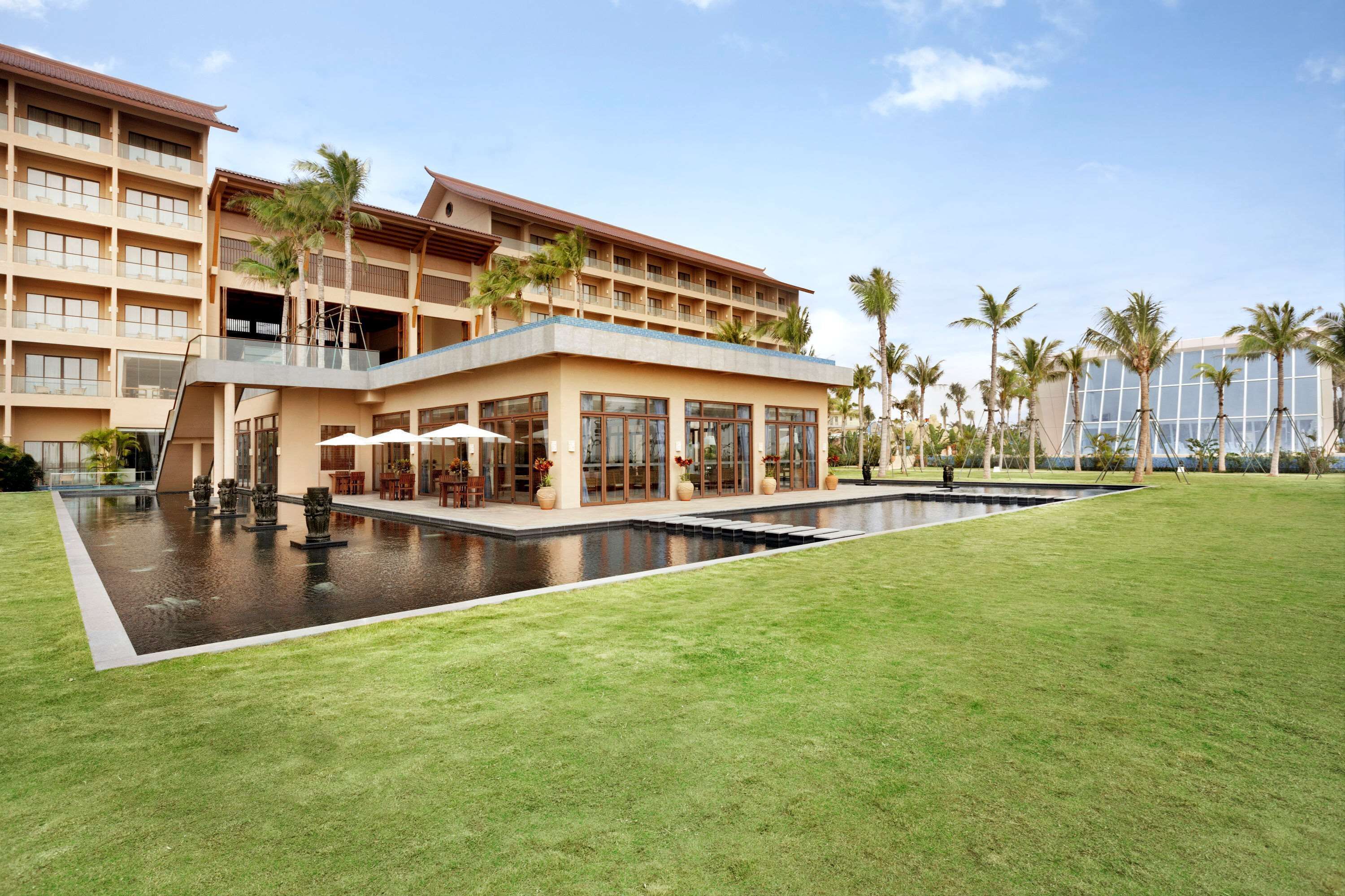 Un hotel con piscina, zona de estar al aire libre y palmeras.