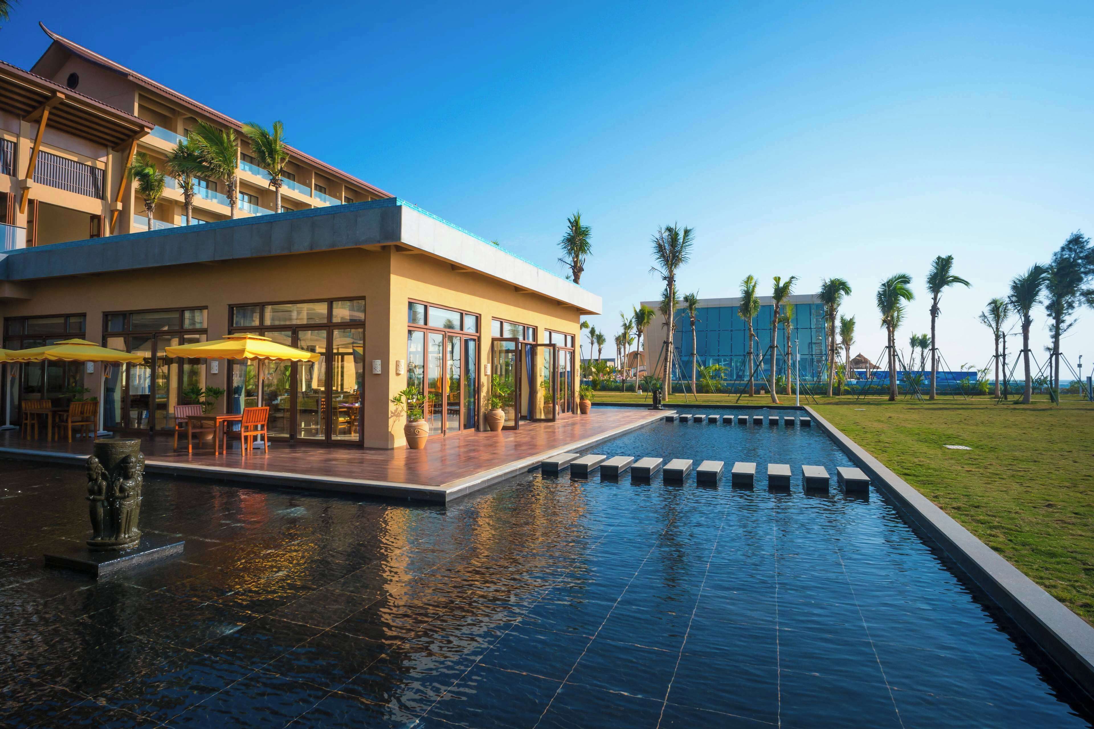 A hotel with a pool area, outdoor seating, and palm trees.