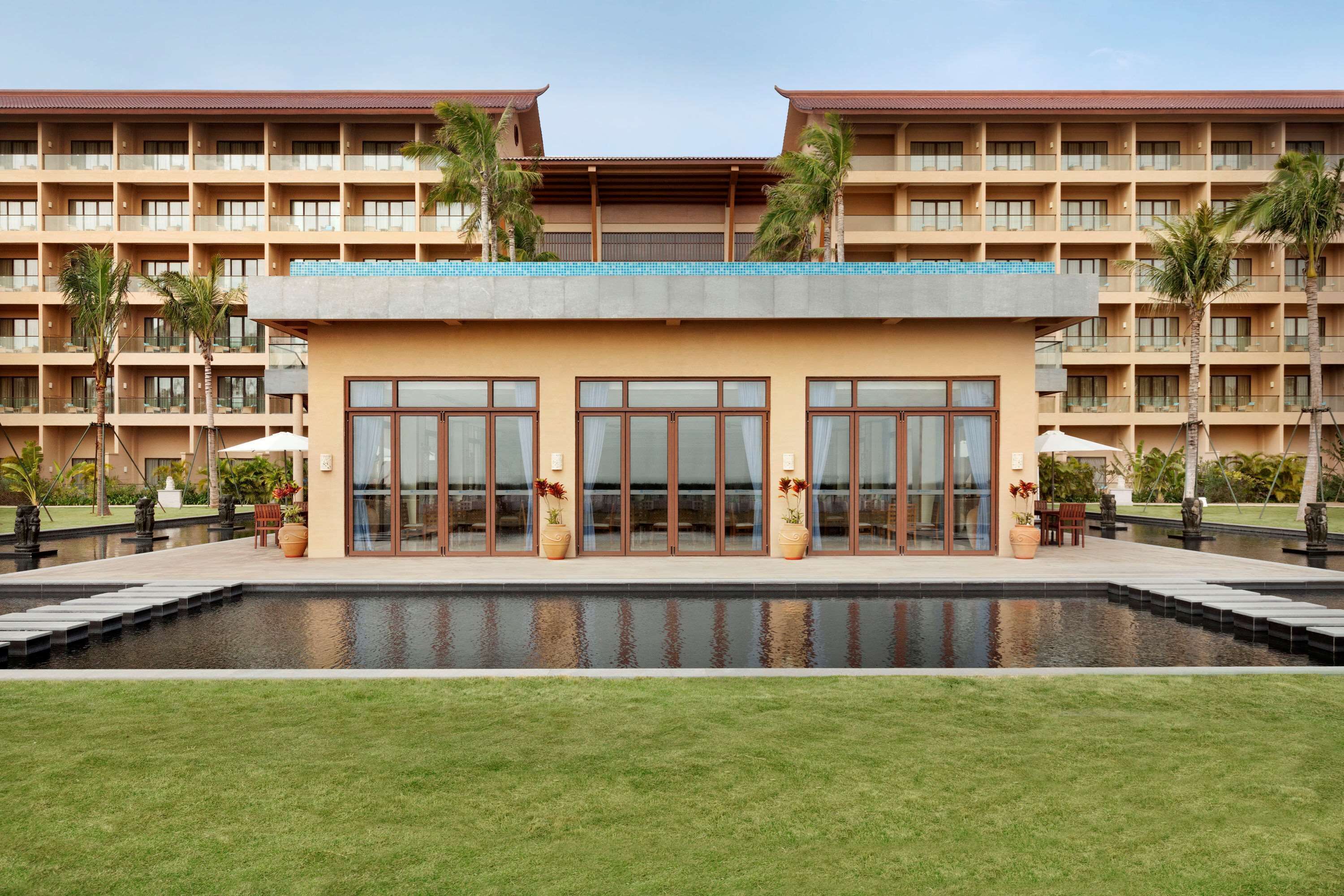 A hotel with a pool, palm trees, and a large building with multiple balconies.