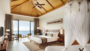Habitación de hotel con una cama grande, un escritorio con silla, televisor y vista al mar.