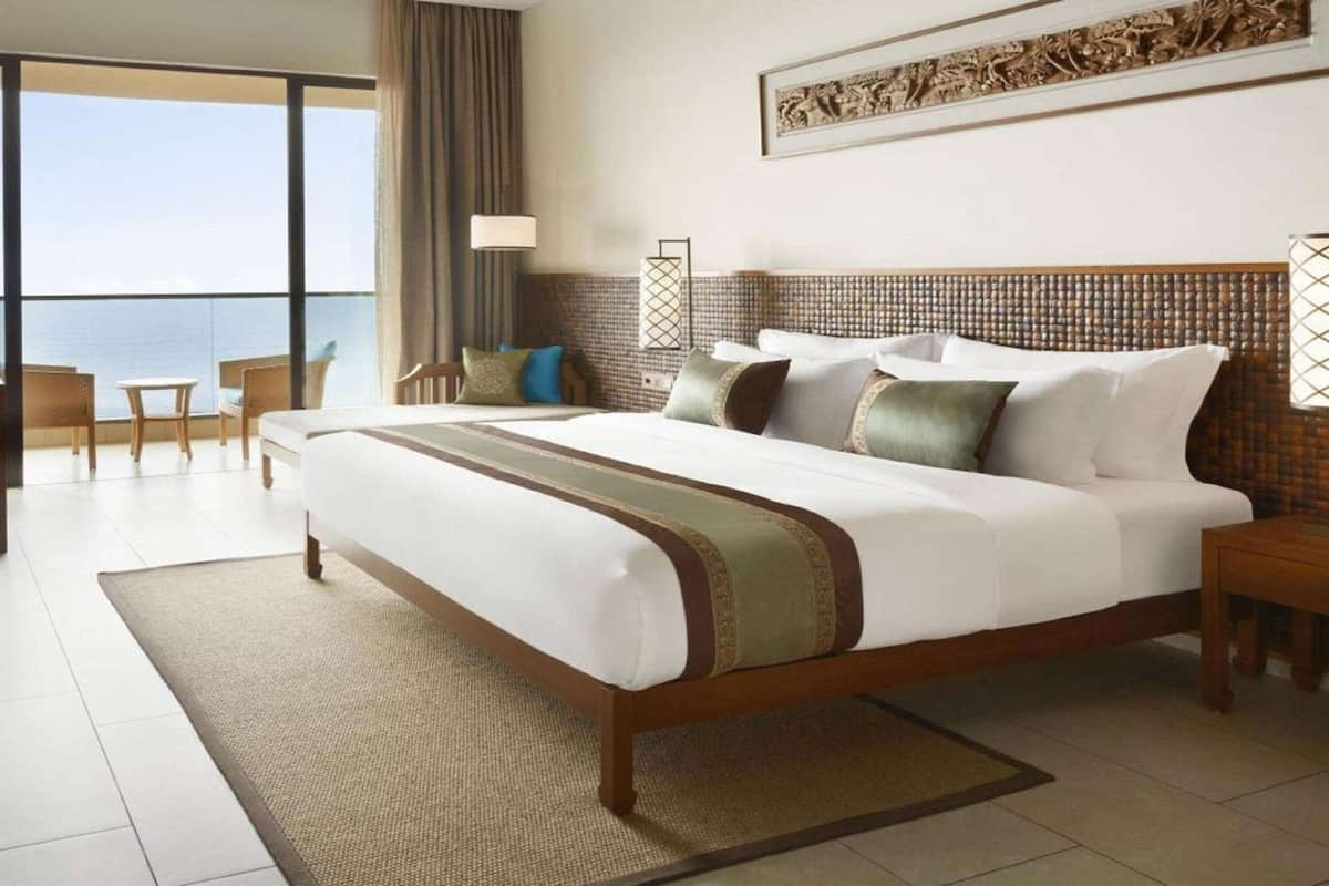 A spacious bedroom with a large bed, a view of the sea, and a balcony with chairs.