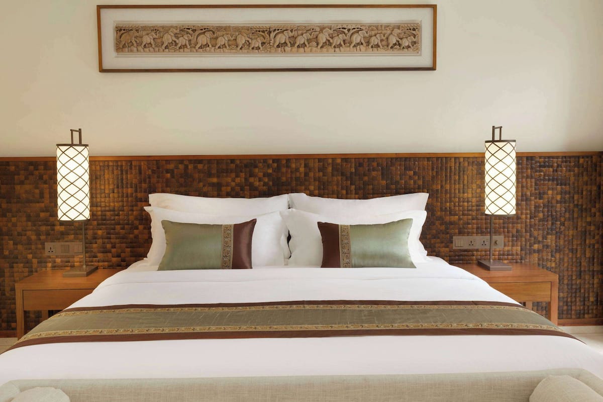 A neatly made bed with white linens and decorative pillows, a wooden headboard, and two bedside lamps.