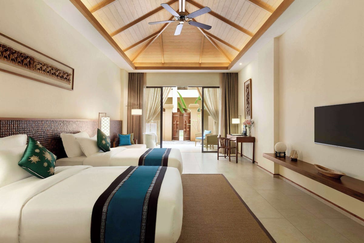 A hotel room with two beds, a ceiling fan, a TV, and a desk with a chair.