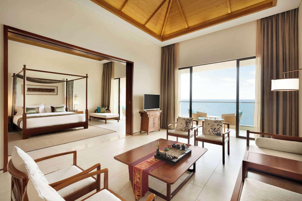 A spacious hotel room with a large bed, a sitting area with a coffee table, and a view of the sea.